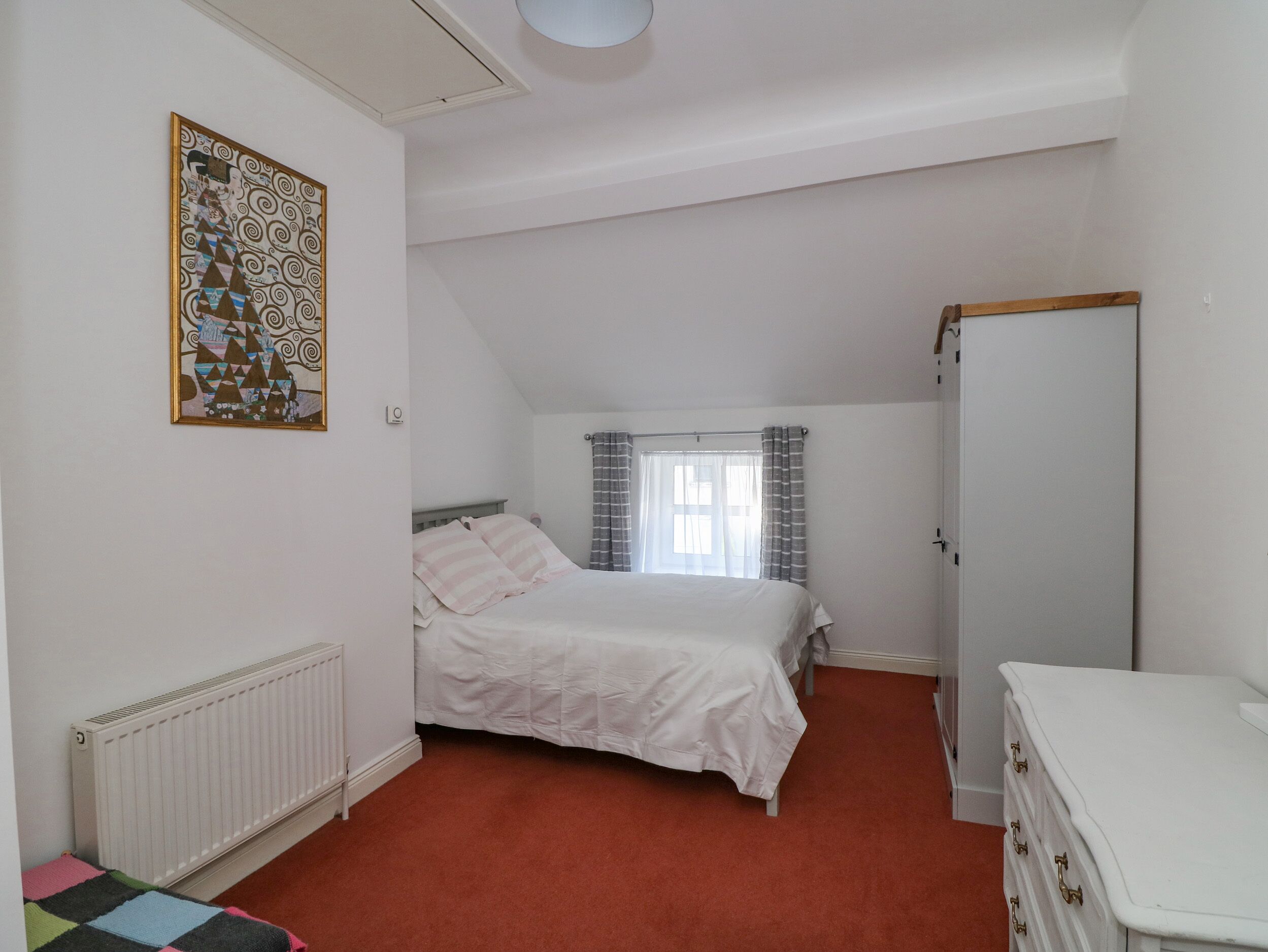 Een slaapkamer met een bed, een radiator, een kledingkast en een raam met gordijnen.