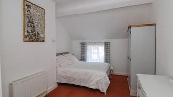 Een slaapkamer met een bed, een radiator, een kledingkast en een raam met gordijnen.