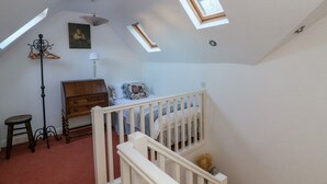 Ein Schlafzimmer mit schräg versiegelter Decke, einem hölzernen Schminktisch, einem Bett mit gemusterten Betttextilien, einer Hängelampe und einem Dachfenster.
