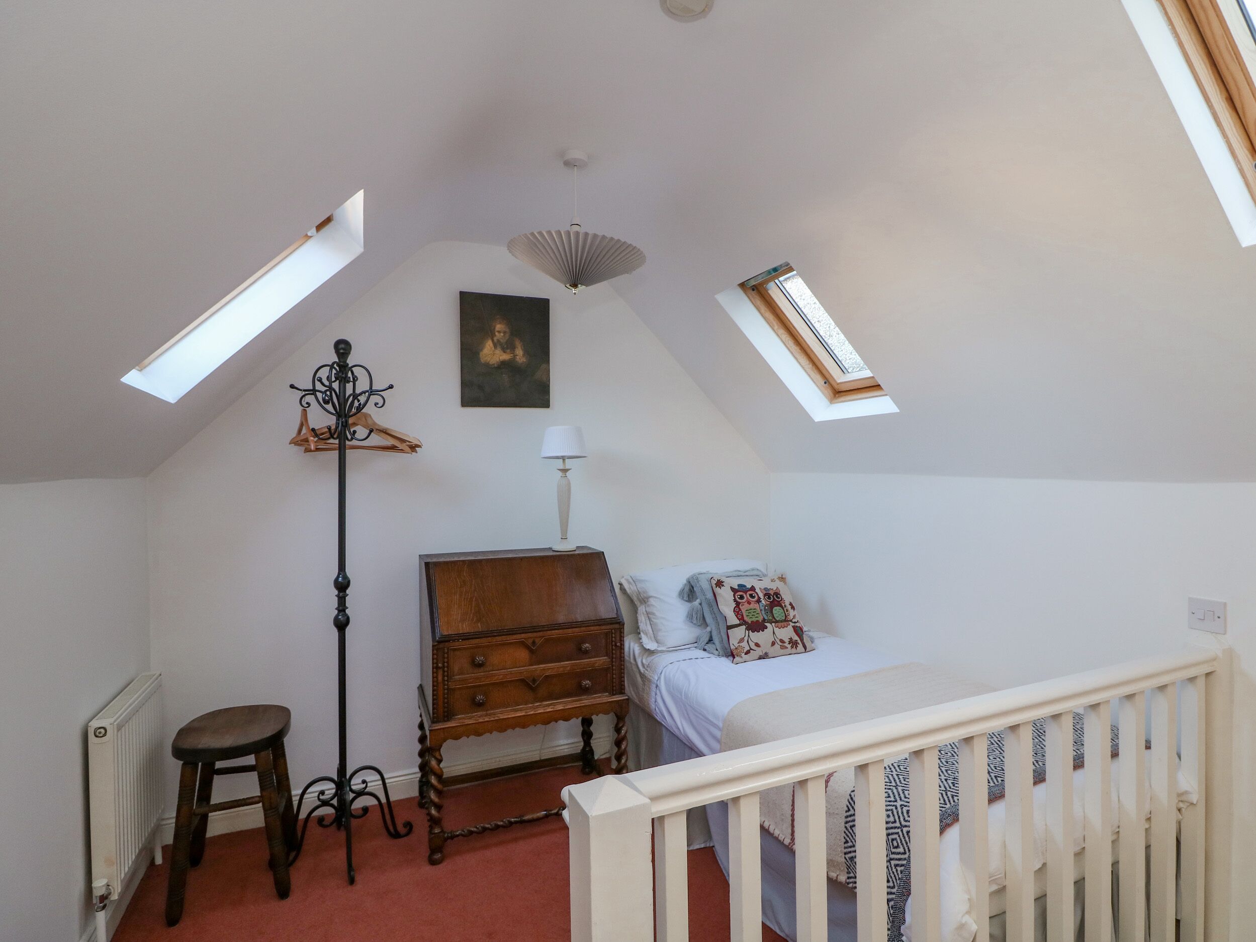 A bedroom with a sloped ceiling, a wooden dresser, a bed with a patterned pillow, a standing lamp, and a radiator.