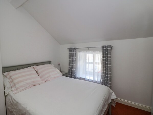 A bedroom with a bed, a window with curtains, and a nightstand with a lamp. - 83 Upper John Street (Wexford)