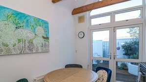Ein Zimmer mit einem runden Holztisch, blauen und grünen Stühlen, einer Wanduhr und einem großen Fenster mit Blick nach draußen.