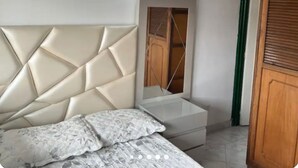 A bedroom with a tufted headboard, a bed with patterned bedding, a bedside table, and a mirror reflecting a wooden wardrobe. - CENTRAL APARTMENT IN POPAYAN (Popayán)