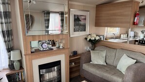 A cozy living area with a fireplace, a sofa, a coffee table, and a bookshelf. - Prestige pet Friendly Caravan on Butlins, Skegness (Skegness)