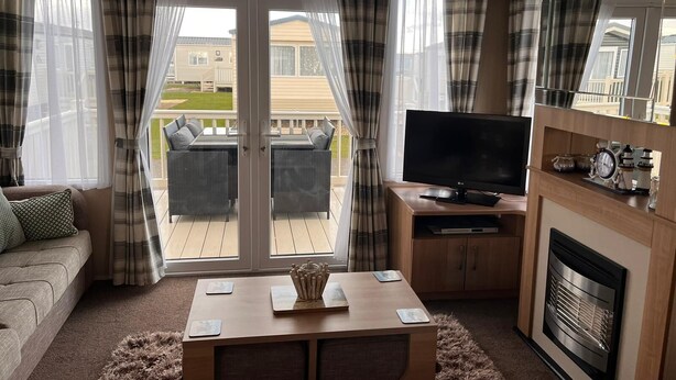 A cozy living room with a TV, a fireplace, and a balcony with curtains. - Prestige pet Friendly Caravan on Butlins, Skegness (Skegness)