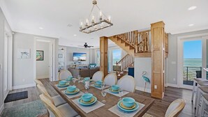 A dining area with a wooden table set for six, a staircase leading to a balcony, and a view of the ocean. - **BLUE HORIZON @ SUGARLOAF SHORES** Home + Last Key White Glove Service... (Sugarloaf Key)
