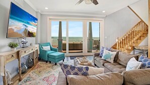 A spacious living room with a large TV, a teal armchair, a sofa with patterned cushions, and a wooden staircase. - **BLUE HORIZON @ SUGARLOAF SHORES** Home + Last Key White Glove Service... (Sugarloaf Key)