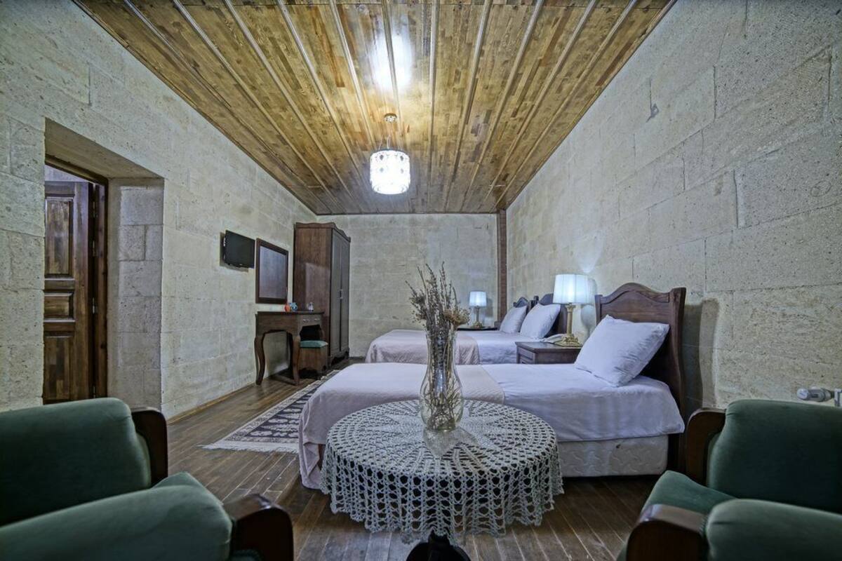 A room with two beds, a wooden ceiling, a round table with a lace tablecloth, and a small cabinet.