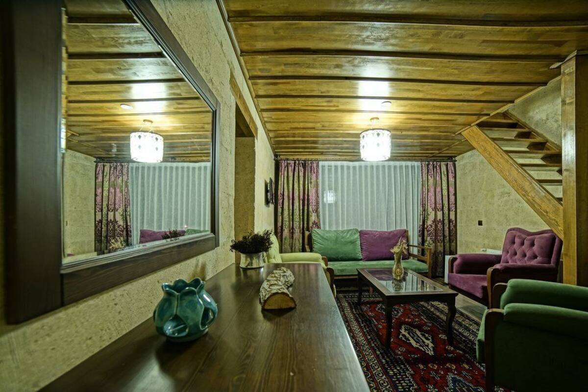 A cozy living room with a wooden ceiling, a large mirror, a sofa, a coffee table, and a staircase.