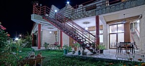 Un edificio de varios niveles con una escalera roja destacada, zona de estar al aire libre y plantas en macetas.