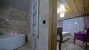 Un baño con pared de piedra, una bañera, zona de ducha y techo de madera.