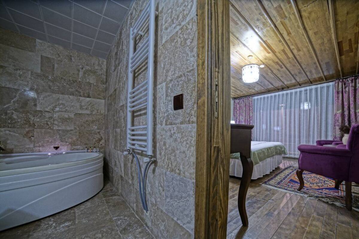A bathroom with a stone wall, a bathtub, a shower area, and a wooden ceiling.