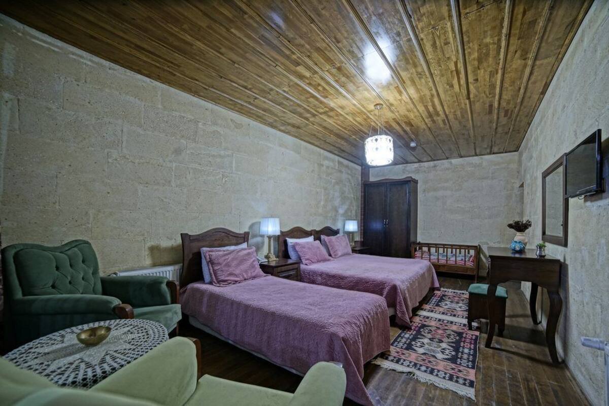 A room with two beds, a wooden ceiling, a brick wall, a small table with a bowl, a chair, a desk with a mirror, and a television.