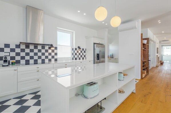 A modern kitchen with white cabinetry, a checkered backsplash, a central island, and a stainless steel range hood.
