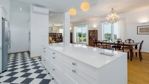 A modern kitchen with a central island, a dining area with a wooden table and chairs, and a chandelier. - Villa Villa Borgonja (Istria - Brtonigla) (Brtonigla)