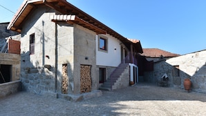 Ein Steinhaus mit Ziegeldach, einer Treppe, die zu einem zweiten Stock führt, und einem Innenhof mit Kopfsteinpflaster.