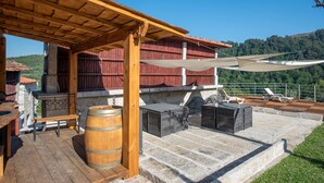 Eine überdachte Terrasse im Freien mit Steinböden, Holzmöbeln und einem großen Fass.