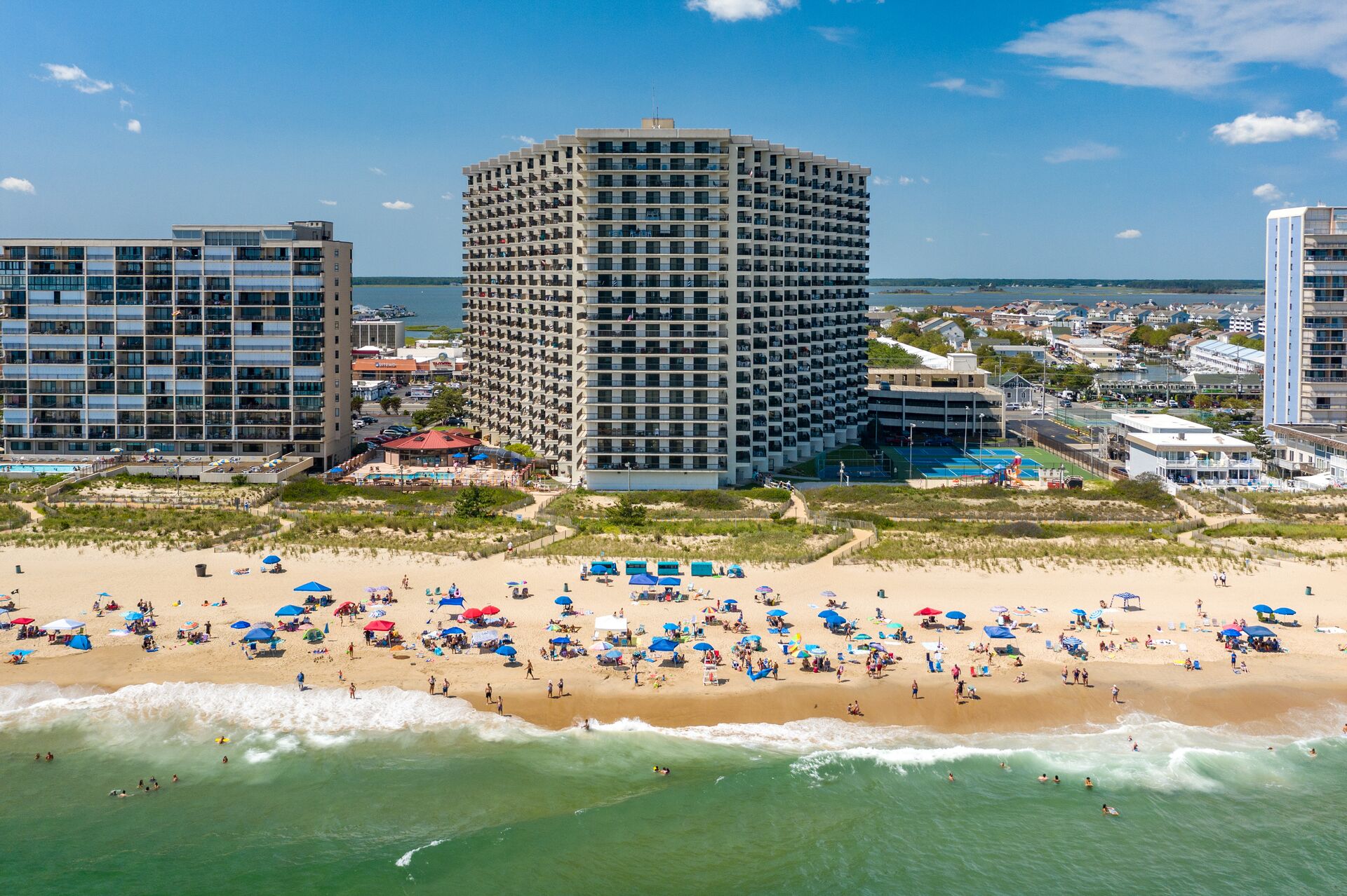 Un hôtel situé en bord de mer, avec plusieurs étages, une piscine et des parasols sur la plage.