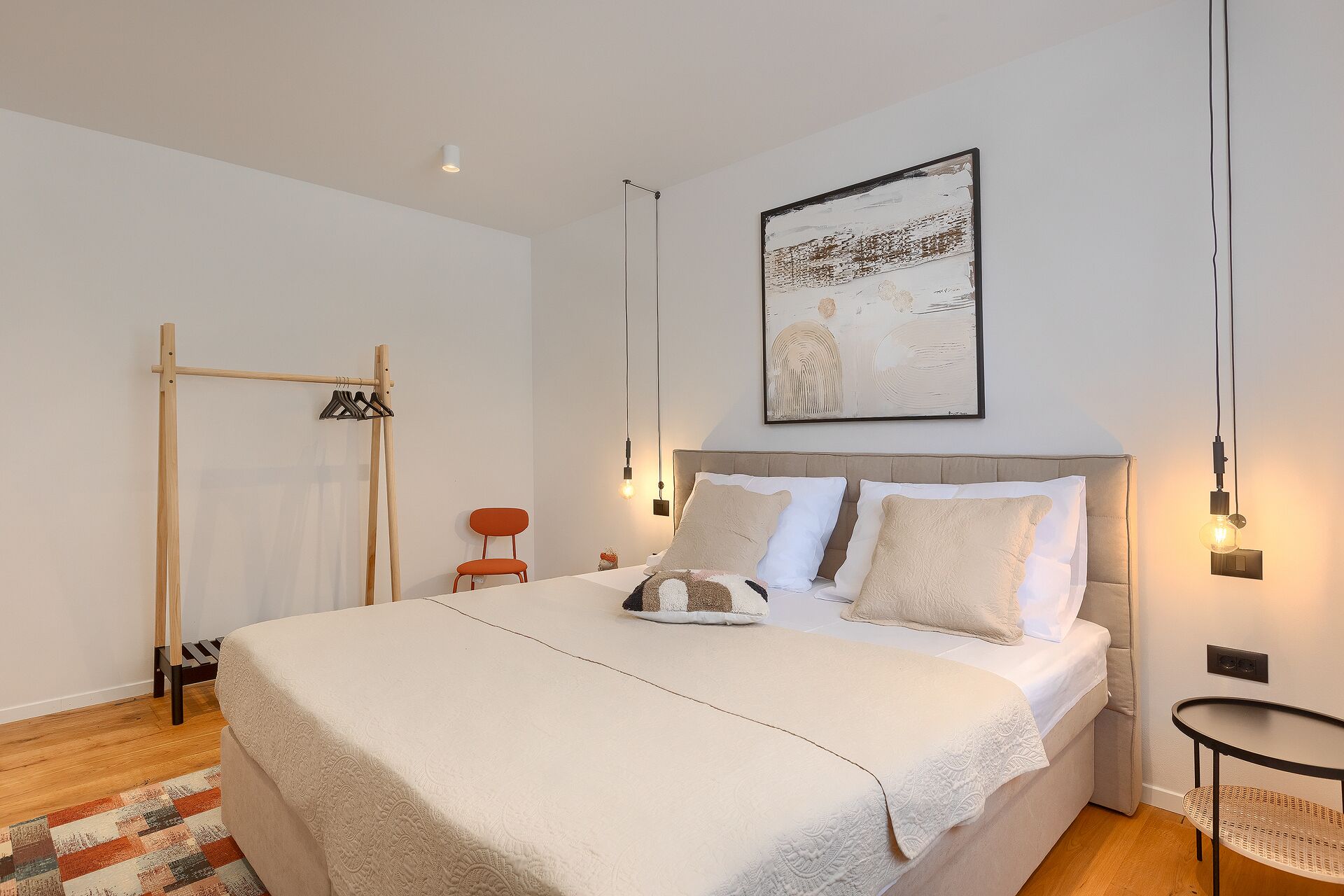 Un dormitorio con una cama grande, un perchero de madera, una silla y un cuadro colgado en la pared.