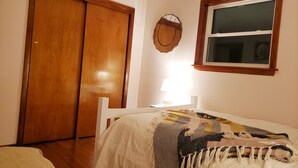 Een slaapkamer met een houten kast, een nachtkastje met een lamp, en een raam met uitzicht.