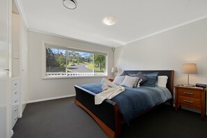 Een slaapkamer met een bed, nachtkastjes, een raam met uitzicht en een deur.