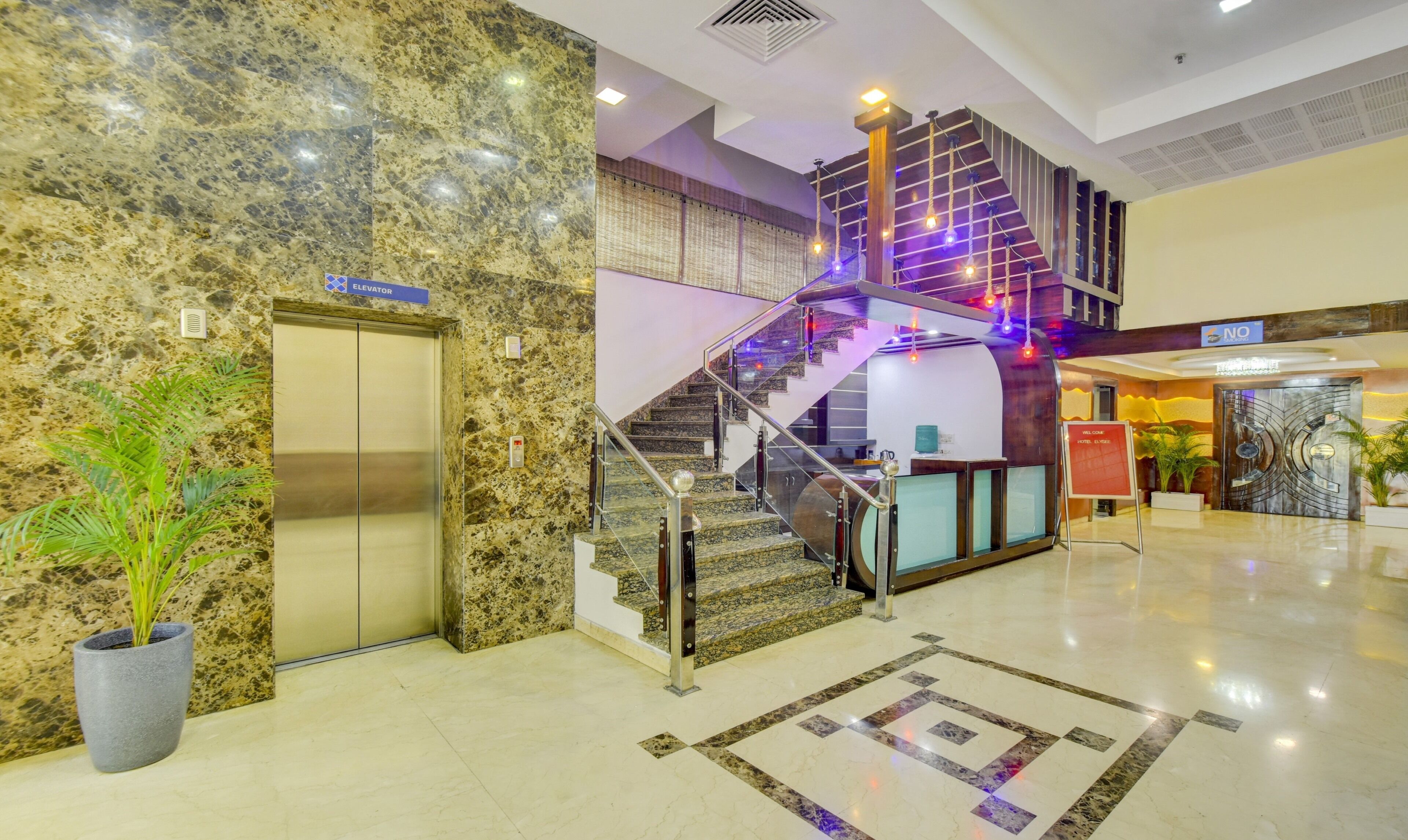 A hotel lobby with a marble reception desk, a staircase with a 'No Entry' sign, and an elevator.