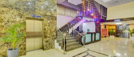 A hotel lobby with a marble reception desk, a staircase with a 'No Entry' sign, and an elevator.