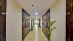 A long, narrow hallway with a polished floor, flanked by dark wooden doors and walls, leading to a bright interior space. - Treebo Elysee, Patel Nagar (Dehradun)
