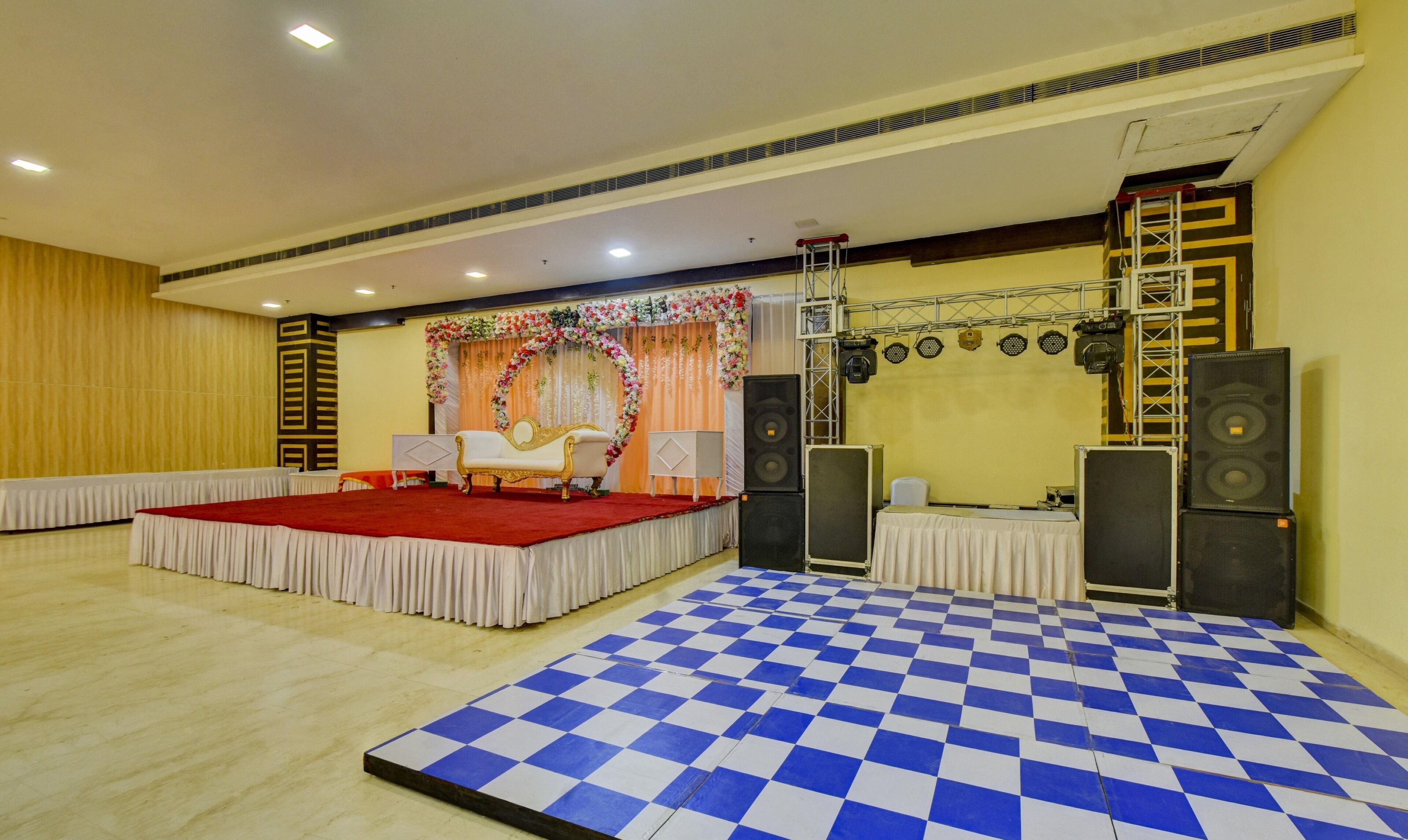 A stage with a red carpet, a white sofa, and a checkered floor. There are speakers and a ladder on the stage.