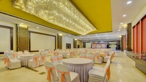A banquet hall with round tables and chairs, a stage with floral decorations, and a modern chandelier. - Treebo Elysee, Patel Nagar (Dehradun)