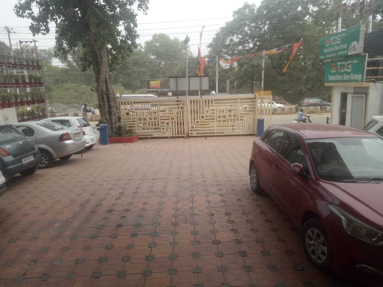 A parking area with cars, a gated entrance, and a building with a sign for 'Travelers Den Group'.