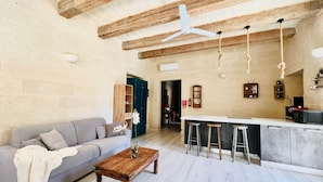A spacious living area with a sofa, a wooden coffee table, and a kitchen area with a bar and stools. - Bright Loft in Center • Near Grand Master Palace  (Valletta)