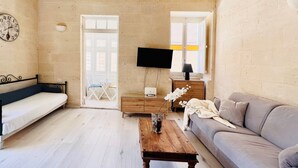A cozy living room with a wooden bench, a sofa, a coffee table, and a TV mounted on the wall. - Bright Loft in Center • Near Grand Master Palace  (Valletta)