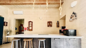 A kitchen with a central island, stools, a microwave, and a fan. - Bright Loft in Center • Near Grand Master Palace  (Valletta)