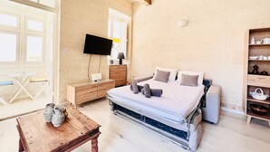 A bedroom with a bed, bedside table, TV, and a wooden cabinet. - Bright Loft in Center • Near Grand Master Palace  (Valletta)