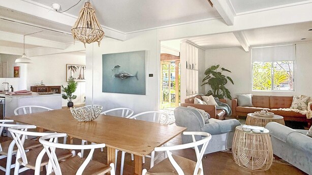 A spacious living area with a wooden dining table, white chairs, a sofa, and a large window. - Tulum Hideaway – Steps to Water, Close to Trails (Callala Bay)