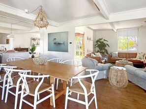 A spacious living area with a wooden dining table, white chairs, a sofa, and a large window. - Tulum Hideaway – Steps to Water, Close to Trails (Callala Bay)