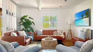 A modern living room with a brown leather sofa, a blue armchair, and a wicker coffee table with books. - Tulum Hideaway – Steps to Water, Close to Trails (Callala Bay)