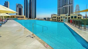 Una piscina en la azotea con barandilla de metal, rodeada de edificios altos y un cielo azul despejado.