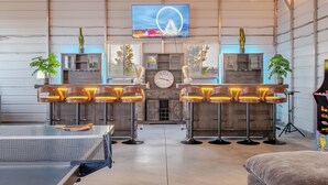 Um espaço amplo de bar com banquetas altas, uma grande tela de TV e um relógio na parede.