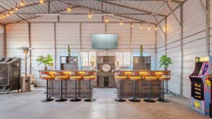 Uma área de bar com quatro banquetas, uma televisão fixada na parede e jogos de arcade.