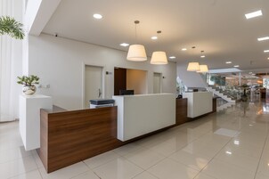 A modern reception area with a wooden reception desk, white walls, and a staircase in the background.