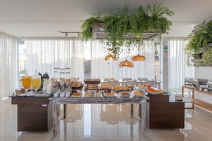 A buffet with various food items and beverages, a coffee station, and hanging plants.