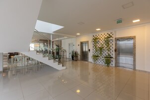 Un vestíbulo de hotel moderno con una escalera de cristal, ascensores y un piso de baldosas impecables.