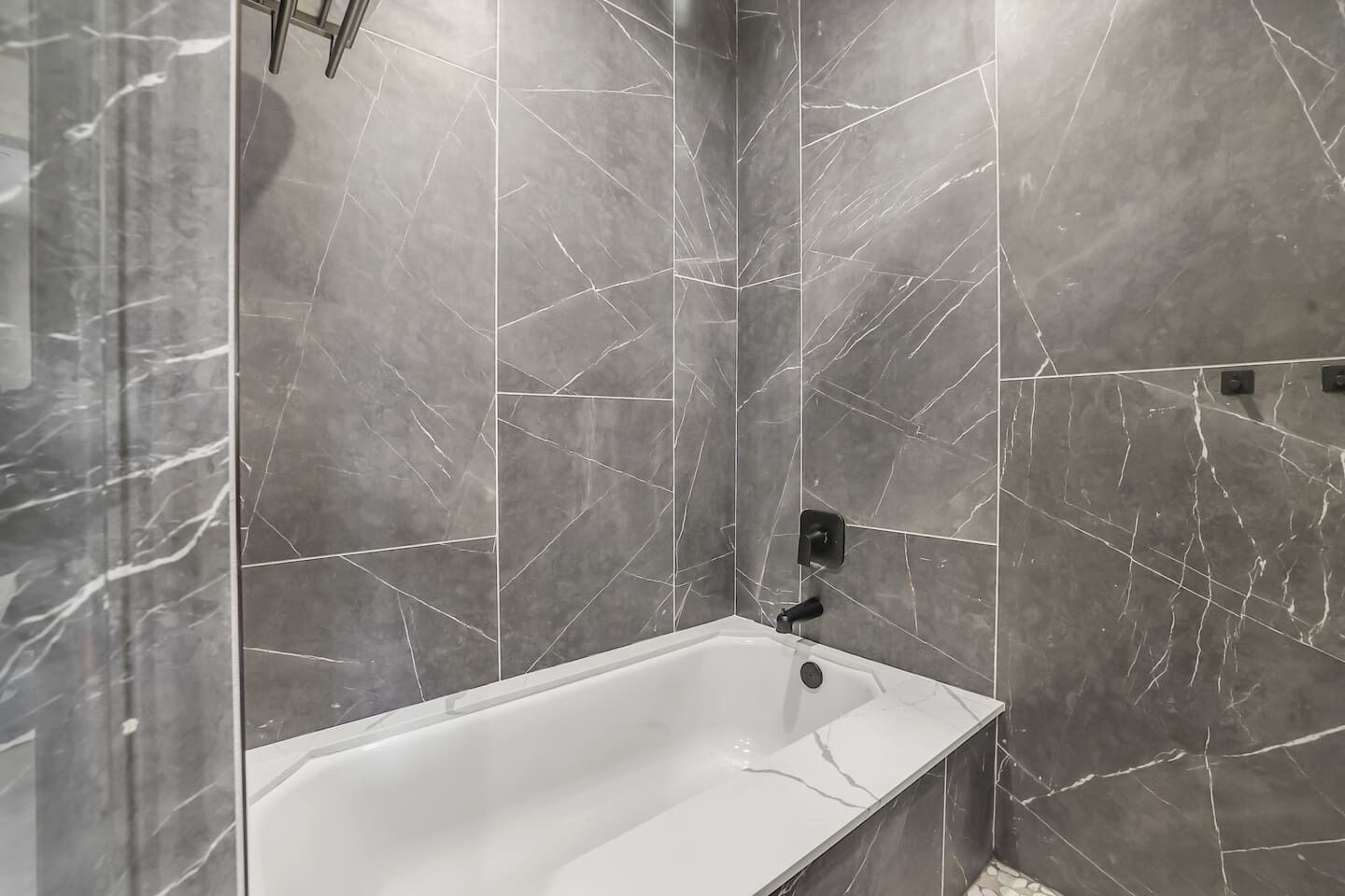Une salle de bain moderne avec une baignoire blanche, des murs en marbre gris et un robinet noir.
