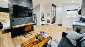 Een moderne woonkamer met een grote flatscreen televisie, een houten salontafel, een bank en een keuken in de achtergrond.