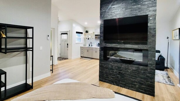 Een moderne woonkamer met een open haard, een keuken op de achtergrond en een grote televisie aan de muur.