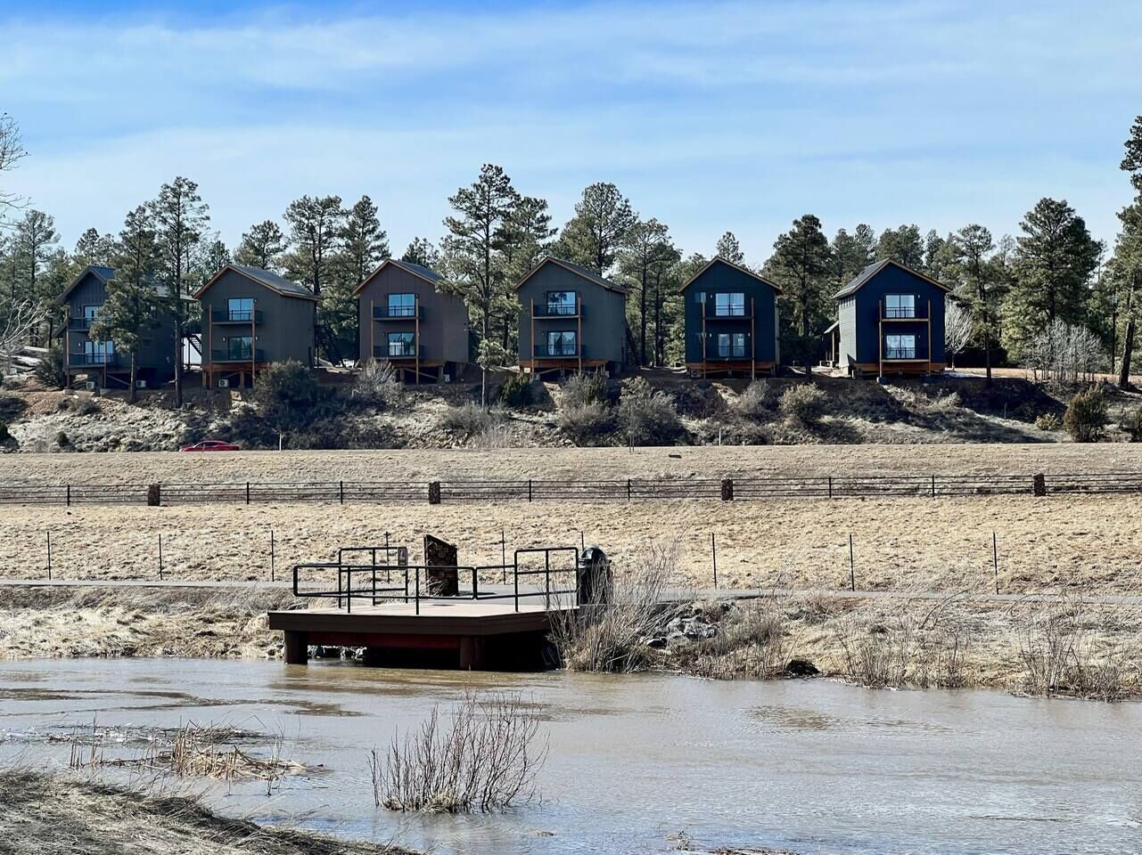 A series of cabins with a dock extending into a body of water, surrounded by a natural landscape.