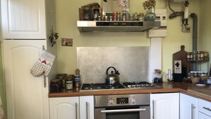 Une cuisine avec des armoires blanches, une cuisinière en acier inoxydable et un four encastré. On peut voir des bocaux et des bouteilles sur le plan de travail, ainsi qu’une bouilloire sur la cuisinière.
