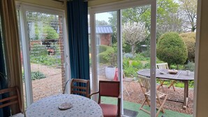 Une pièce avec une table ronde et des chaises, une grande porte-fenêtre coulissante donnant sur un jardin où se trouvent une table et des chaises en bois.